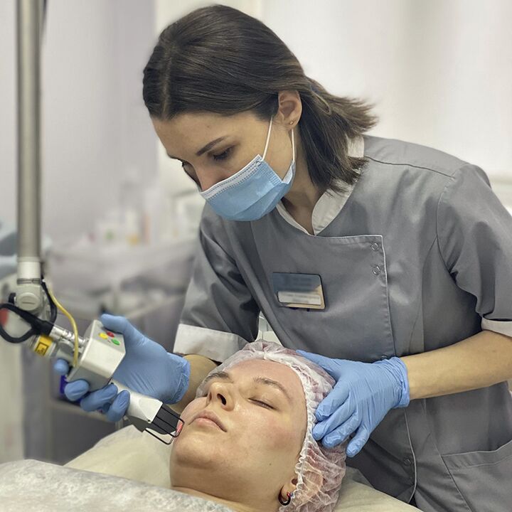 A cosmetologist performs a fractional laser rejuvenation procedure of facial skin